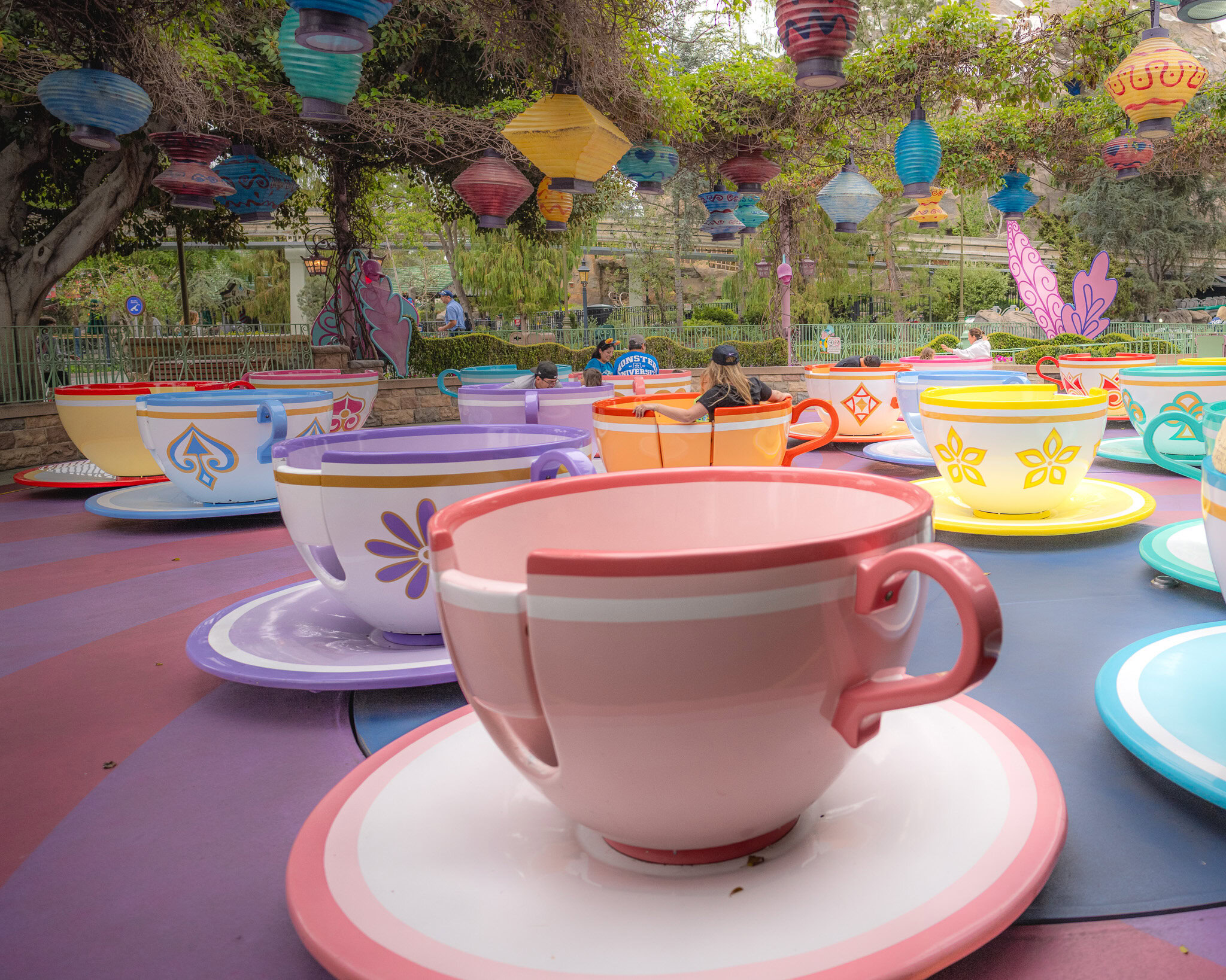 Colorful teacups on the Mad Tea Party ride at Disneyland, surrounded by whimsical lanterns and trees.
