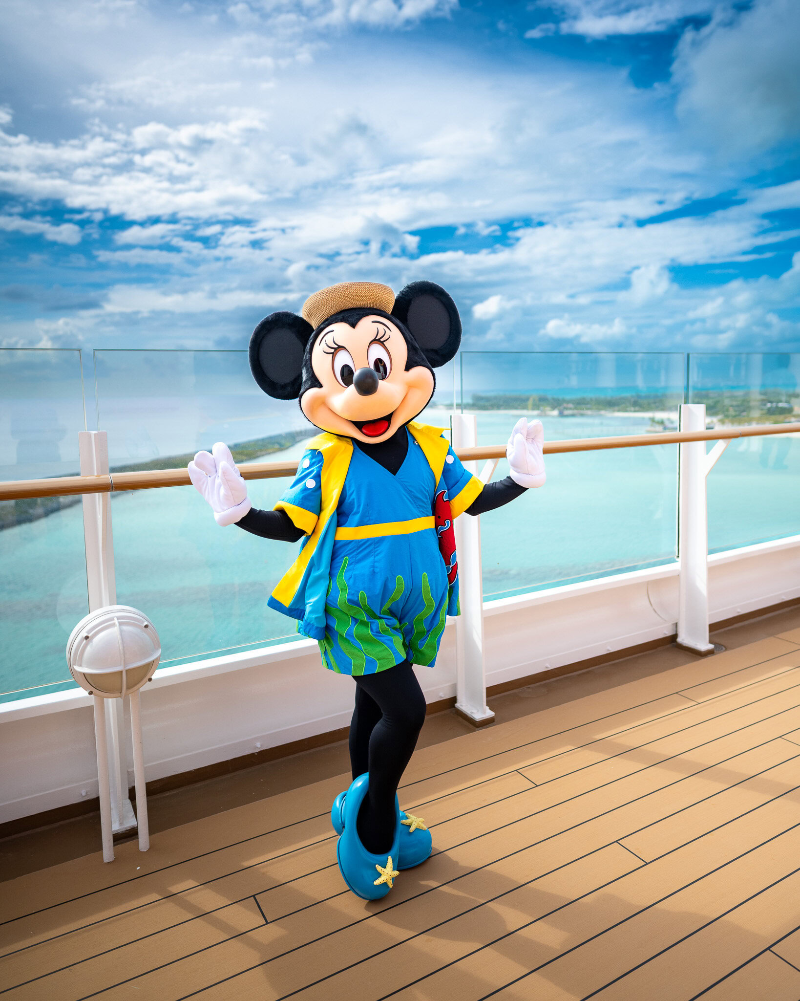 Minnie Mouse posing on the top deck of the Disney Fantasy with Castaway Cay in the background.