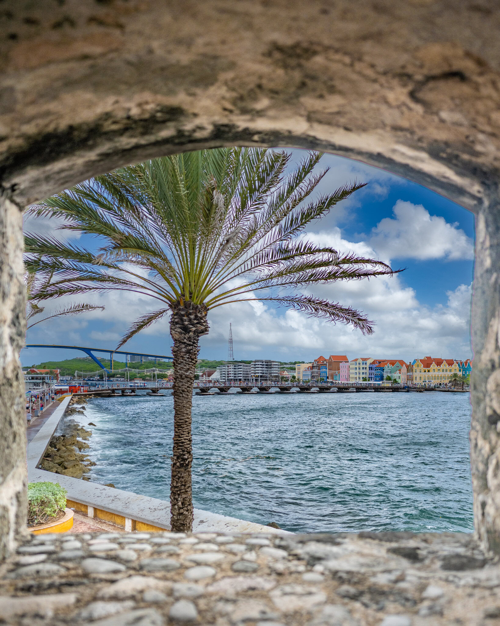 Curacao waterfront with colorful Dutch buildings and palm tree viewed from stone arch during a Southern Caribbean Disney Cruise