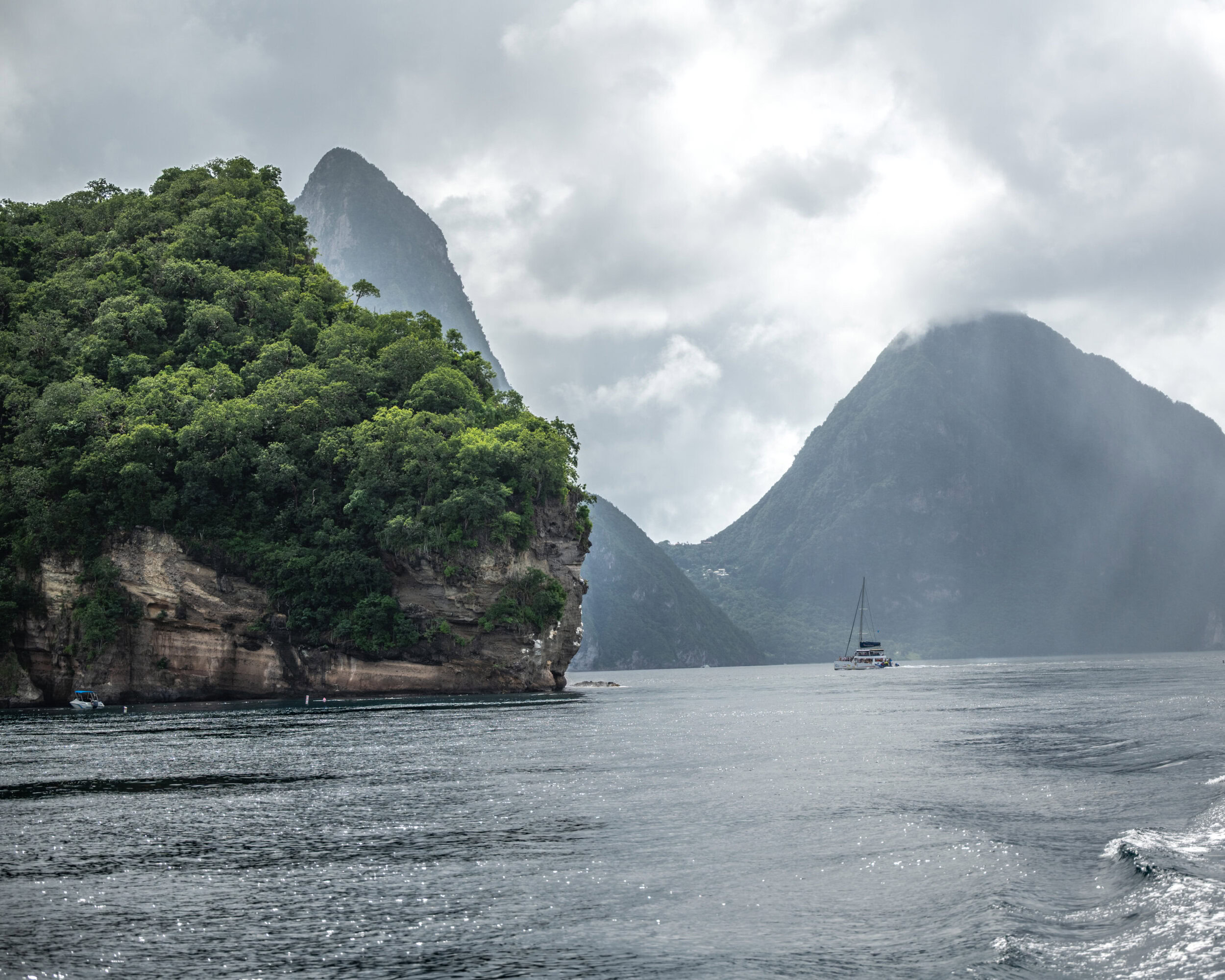Catamaran sailing near the Pitons mountains in St. Lucia with overcast skies.
