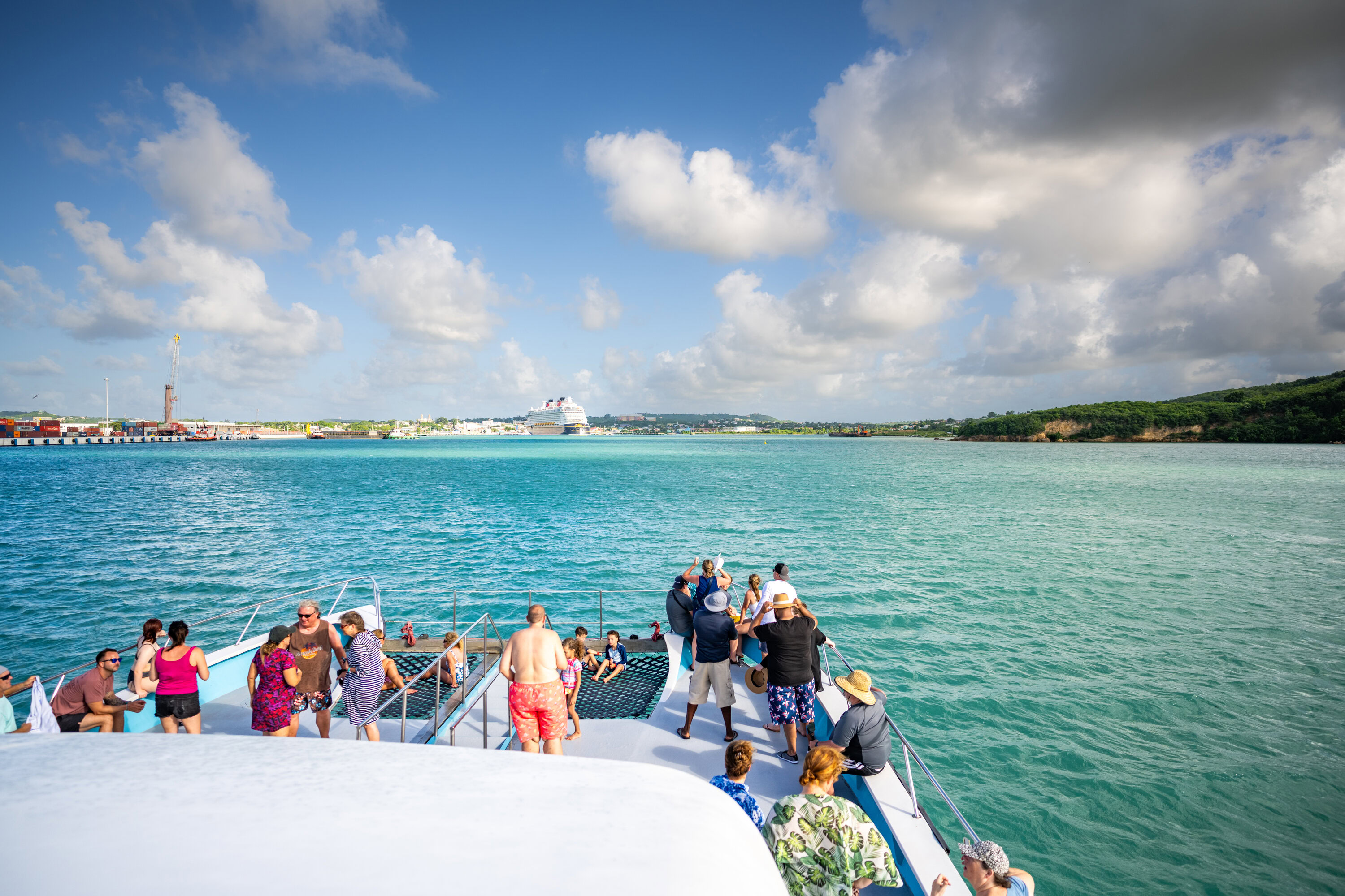 Catamaran with passengers sailing toward Antigua’s port with Disney Magic docked.