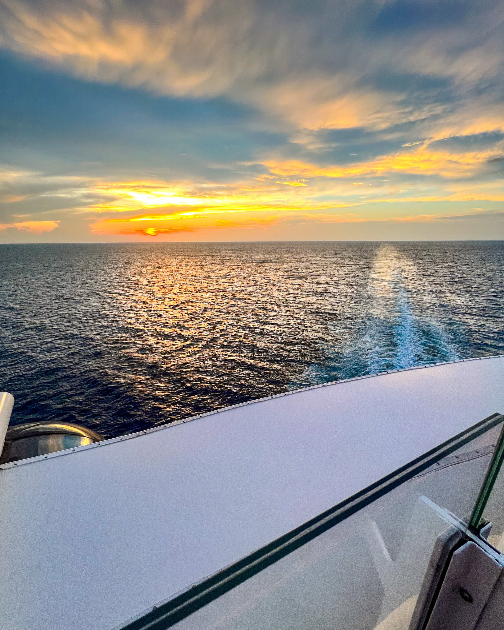 Ocean sunset view from the deck of a Disney cruise ship with golden clouds and blue waters.
