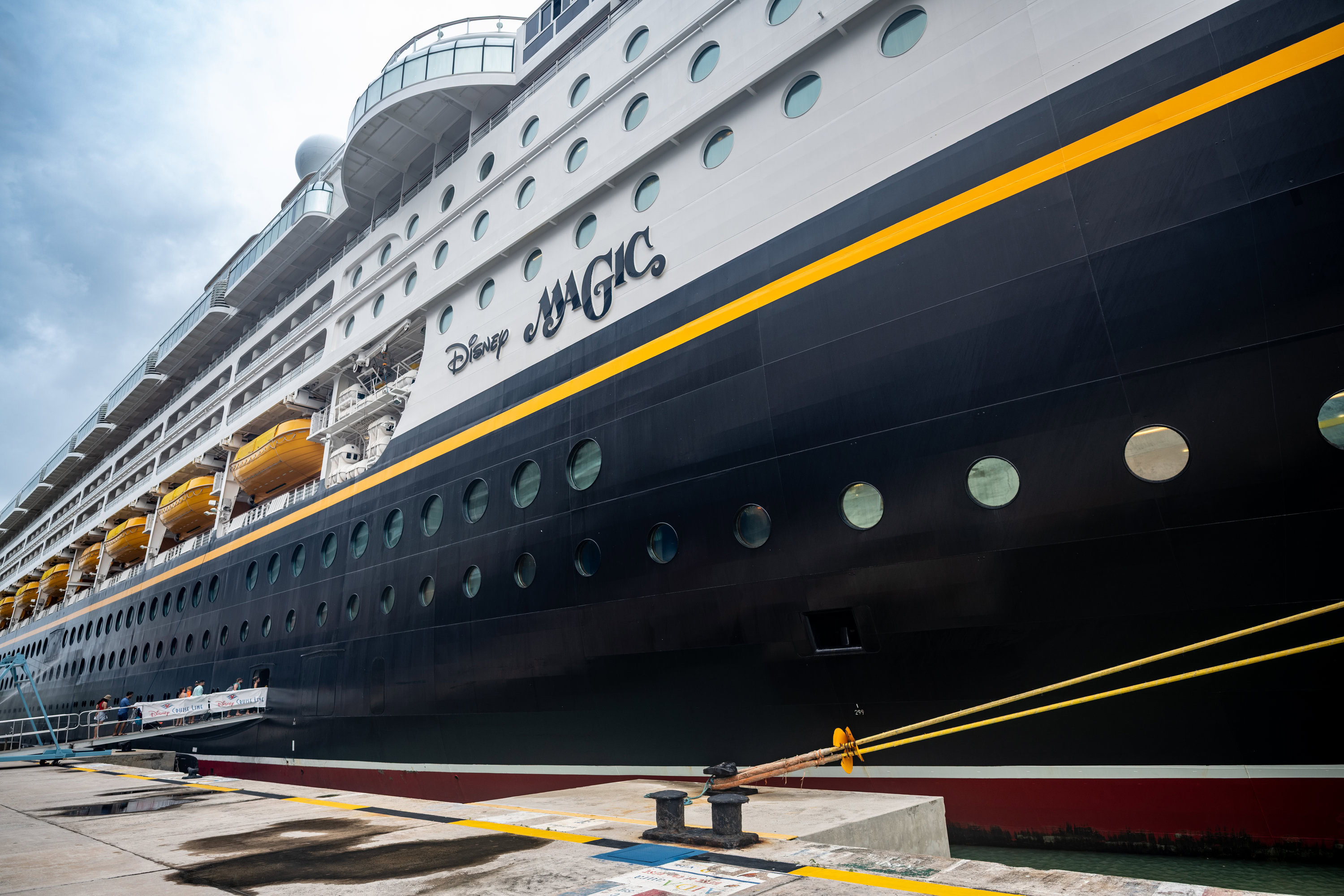 Side view of Disney Magic cruise ship docked in Antigua port on a cloudy day.