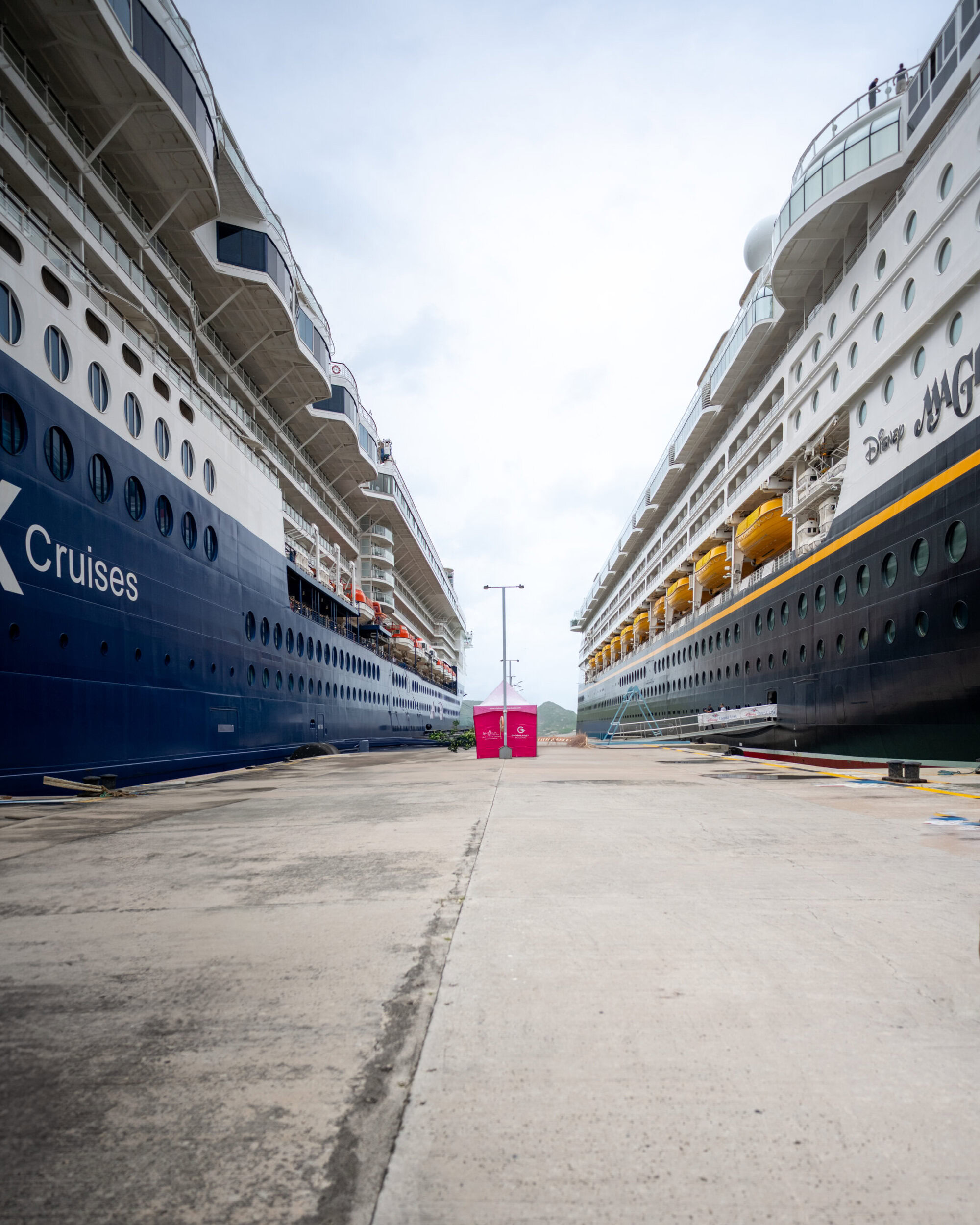 Disney Magic cruise ship docked next to Celebrity Cruises vessel in Antigua port.