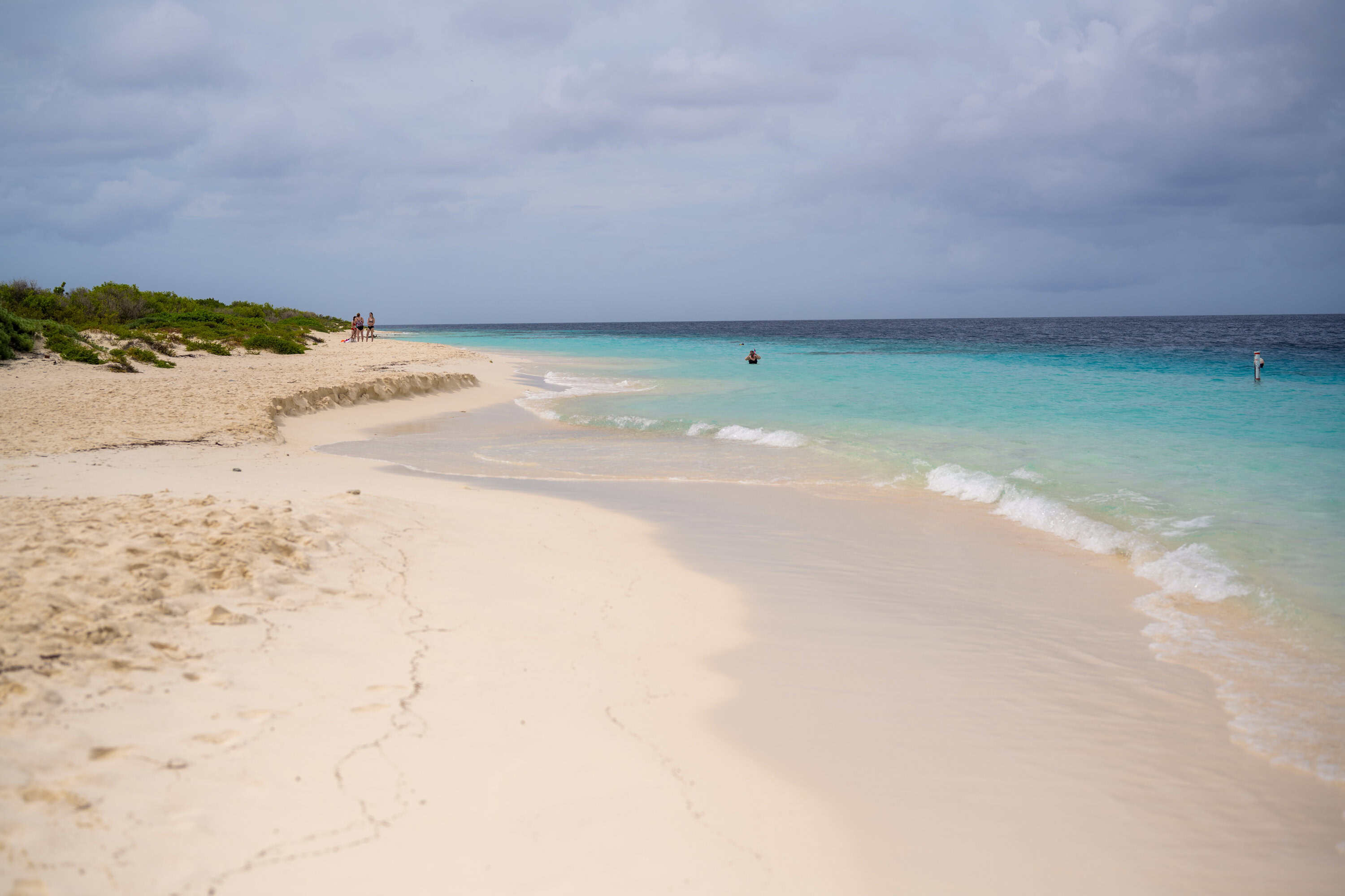 White sandy beach and turquoise sea at Klein Bonaire under partly cloudy skies.