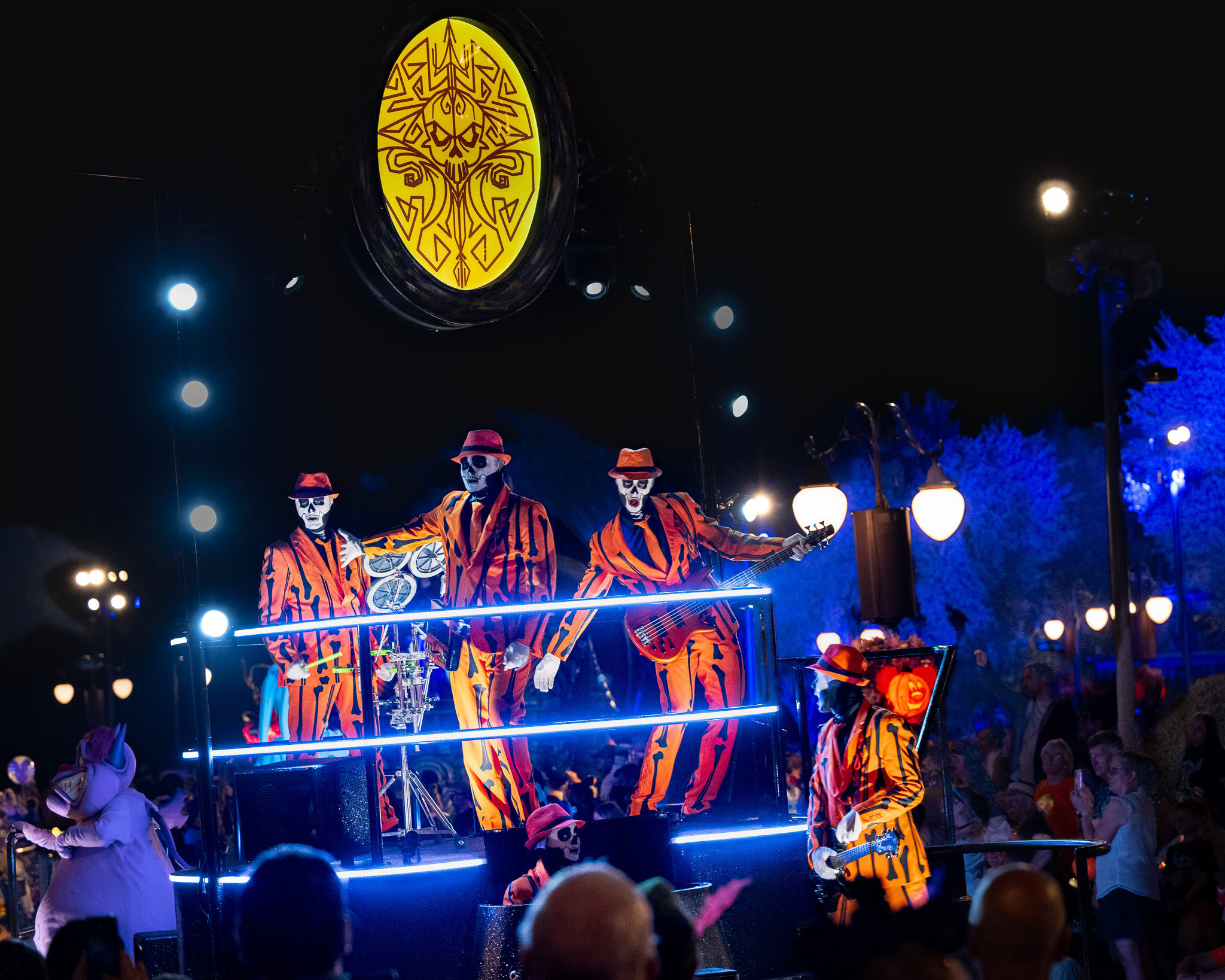 Skeleton band performers in bright orange striped suits playing instruments on a glowing float during Mickey’s Not-So-Scary Halloween Party parade at Magic Kingdom.