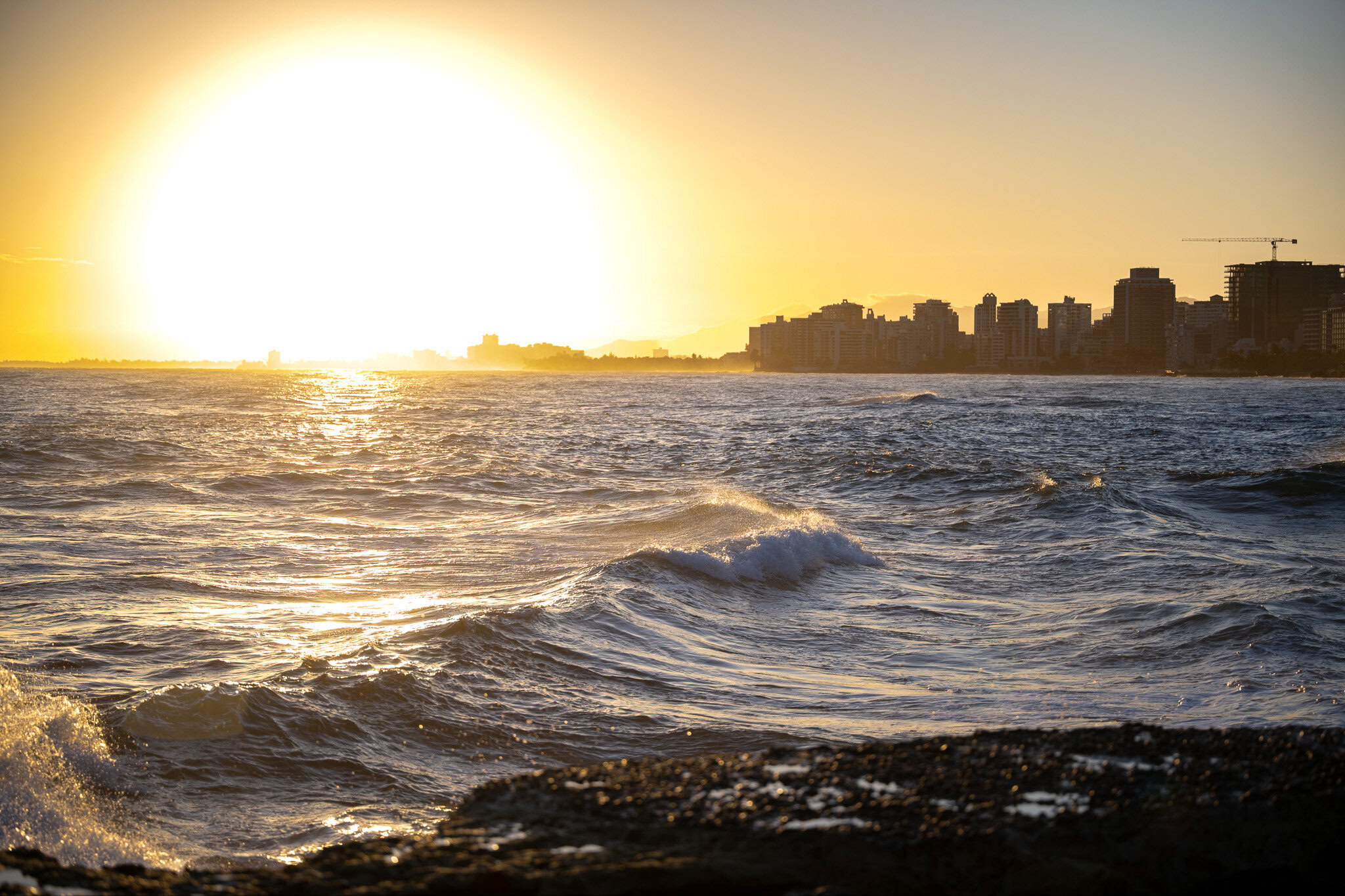 Sunset over waves at Escambr&oacute;n Beach in San Juan, Puerto Rico with the city skyline in the background.