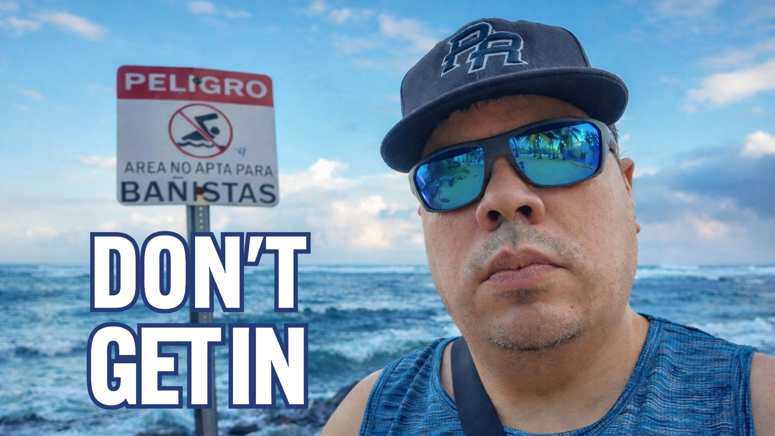 Man standing near rough ocean waves in San Juan next to a &ldquo;PELIGRO&rdquo; sign warning that the area is not safe for swimmers.
