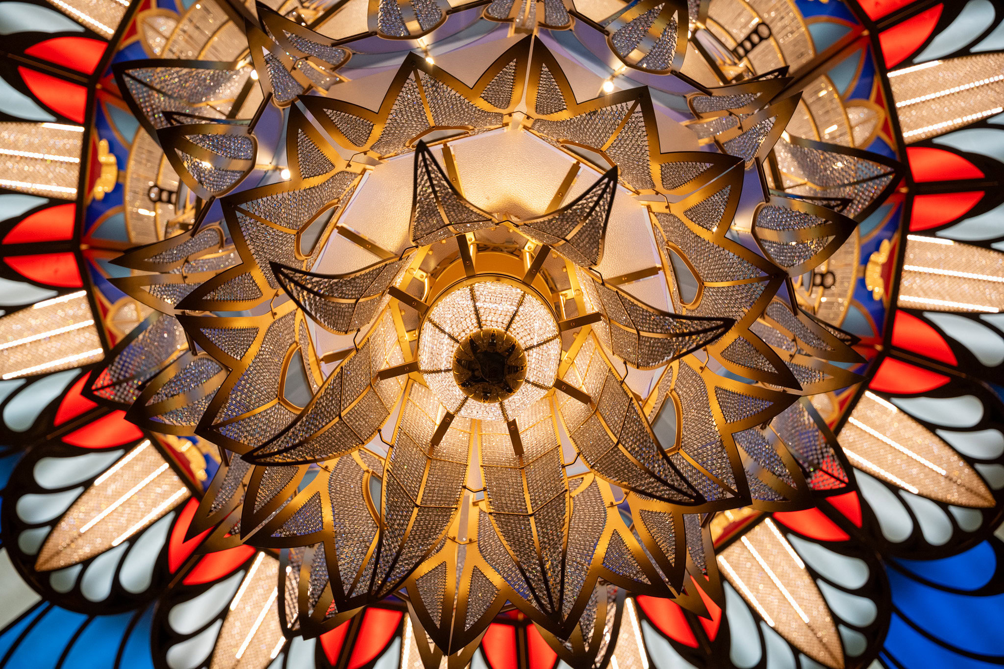 Close-up of the ornate chandelier on the Disney Dream cruise ship with gold accents, crystals, and stained-glass red, blue, and white patterns. Photo by Raúl Colón, Photographer and Travel Advisor.