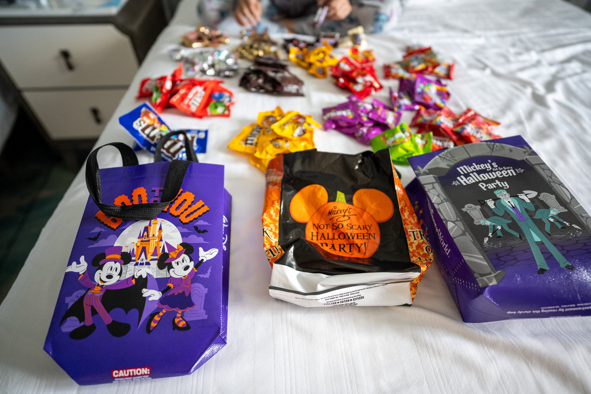 Mickey’s Not-So-Scary Halloween Party candy spread across a bed at Disney’s Grand Floridian Resort, with Halloween treat bags from Magic Kingdom.