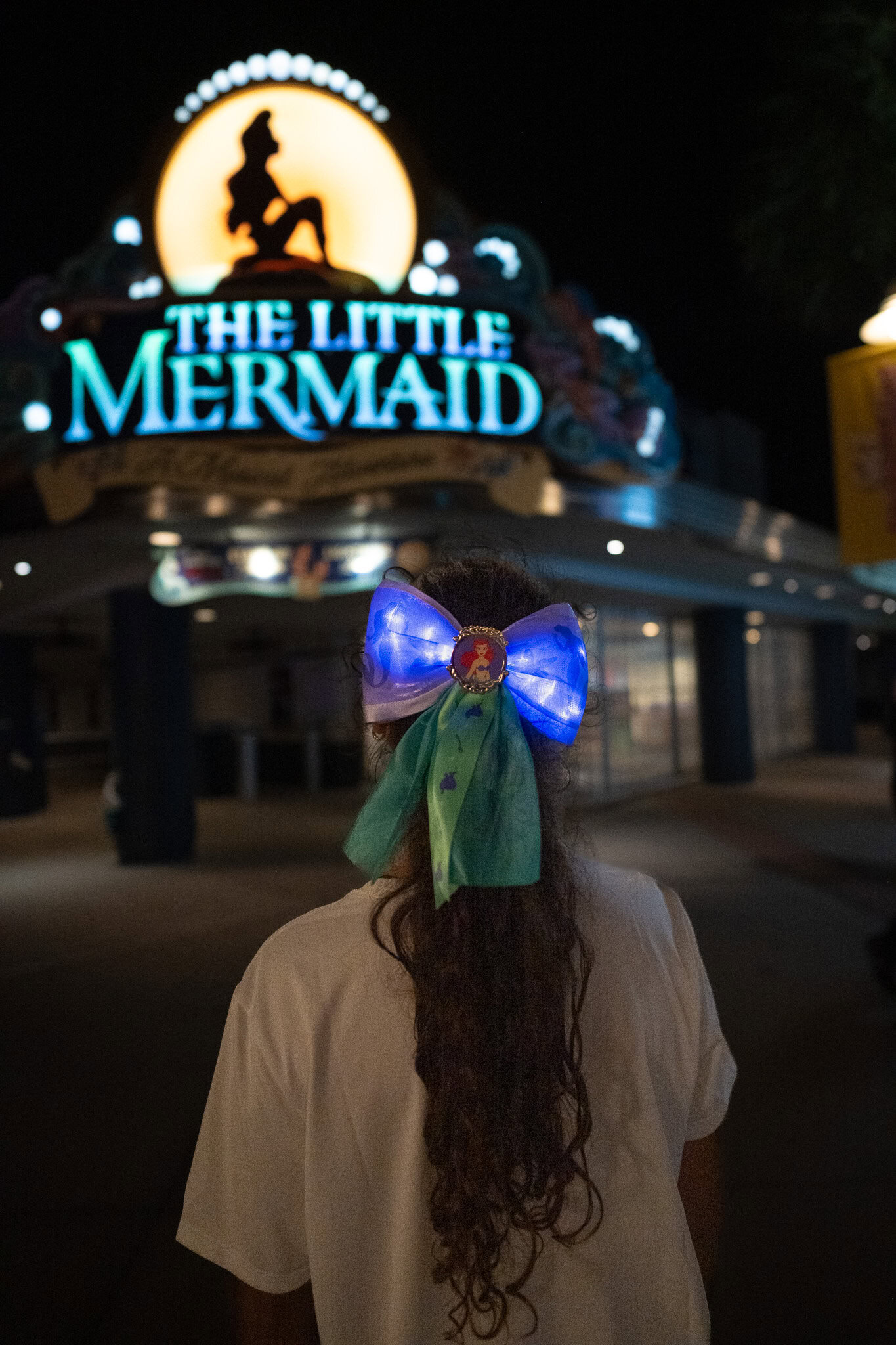 Martina wearing Little Mermaid bow walking toward The Little Mermaid attraction at night