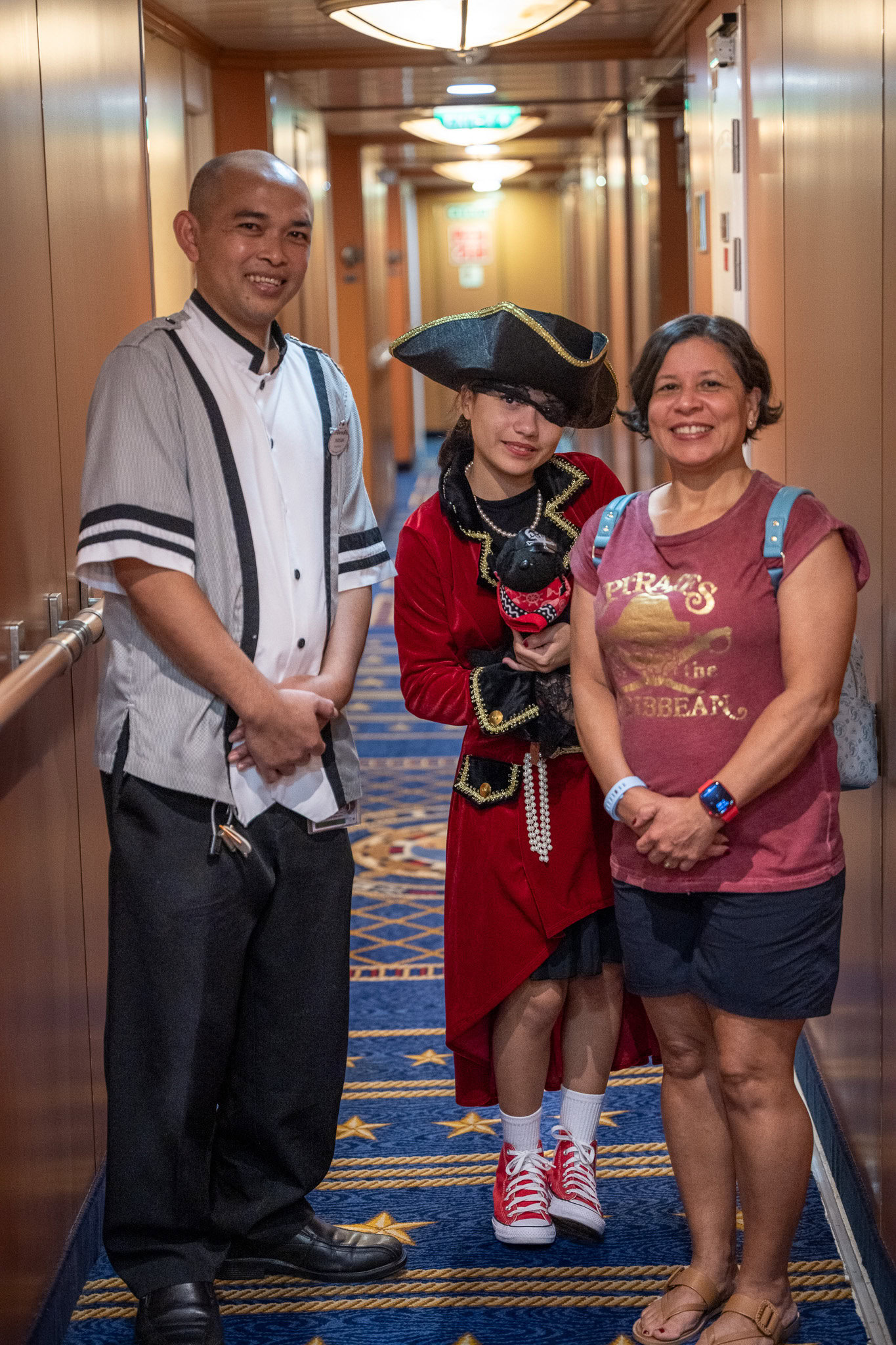 Disney Magic room attendant Wayan posing with cruise guests in a ship corridor.
