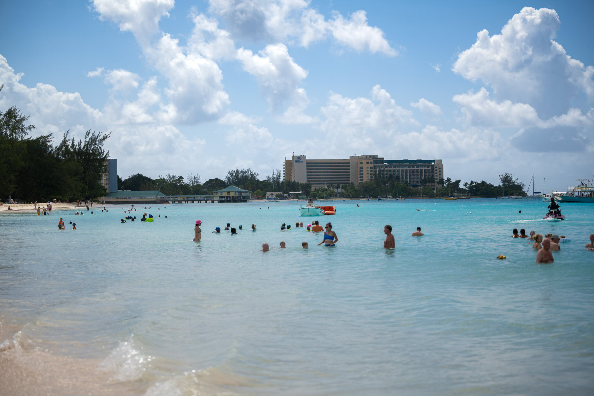Visitors enjoying the shallow turquoise water at Harbour Lights Beach in Carlisle Bay, Barbados.