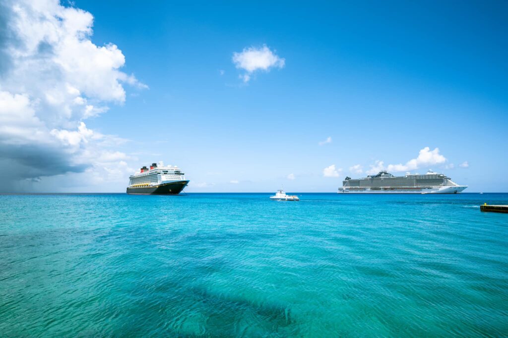 Disney Fantasy docked off the coast of Grand Cayman with clear blue waters and another cruise ship in view.