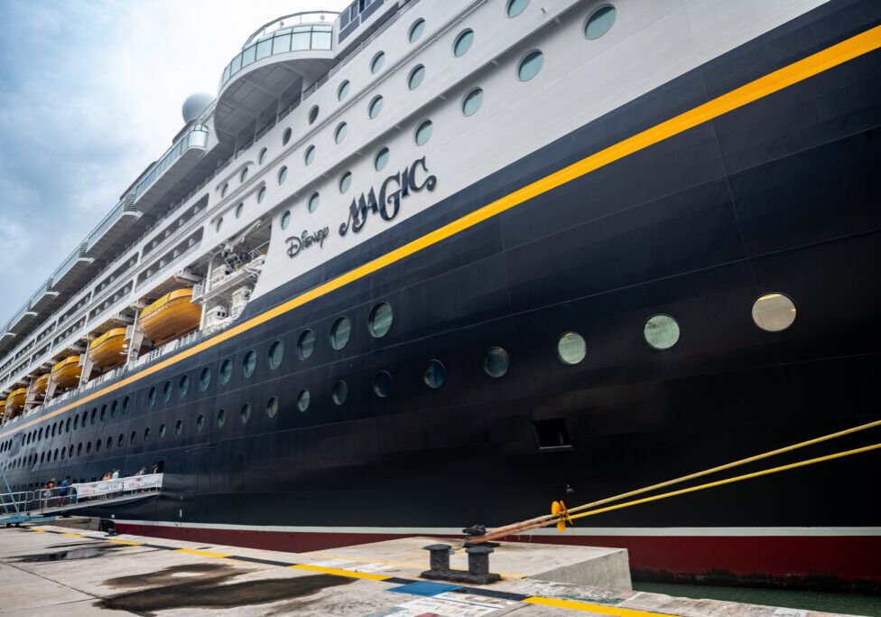 Side view of Disney Magic cruise ship docked in Antigua port on a cloudy day.