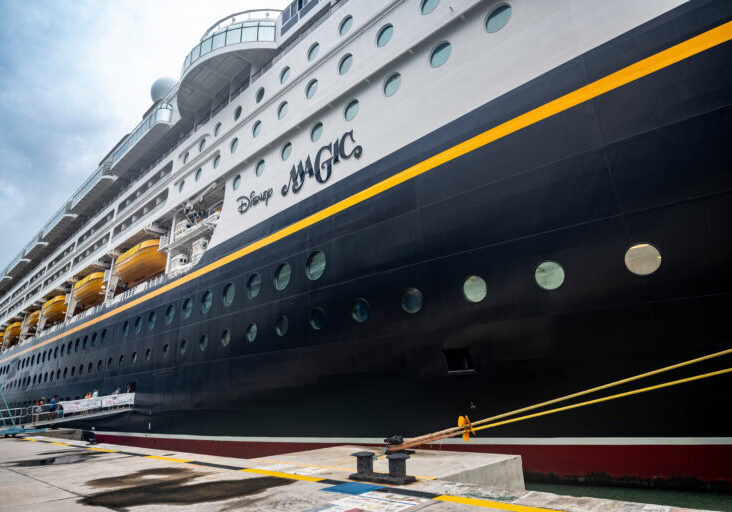 Side view of Disney Magic cruise ship docked in Antigua port on a cloudy day.