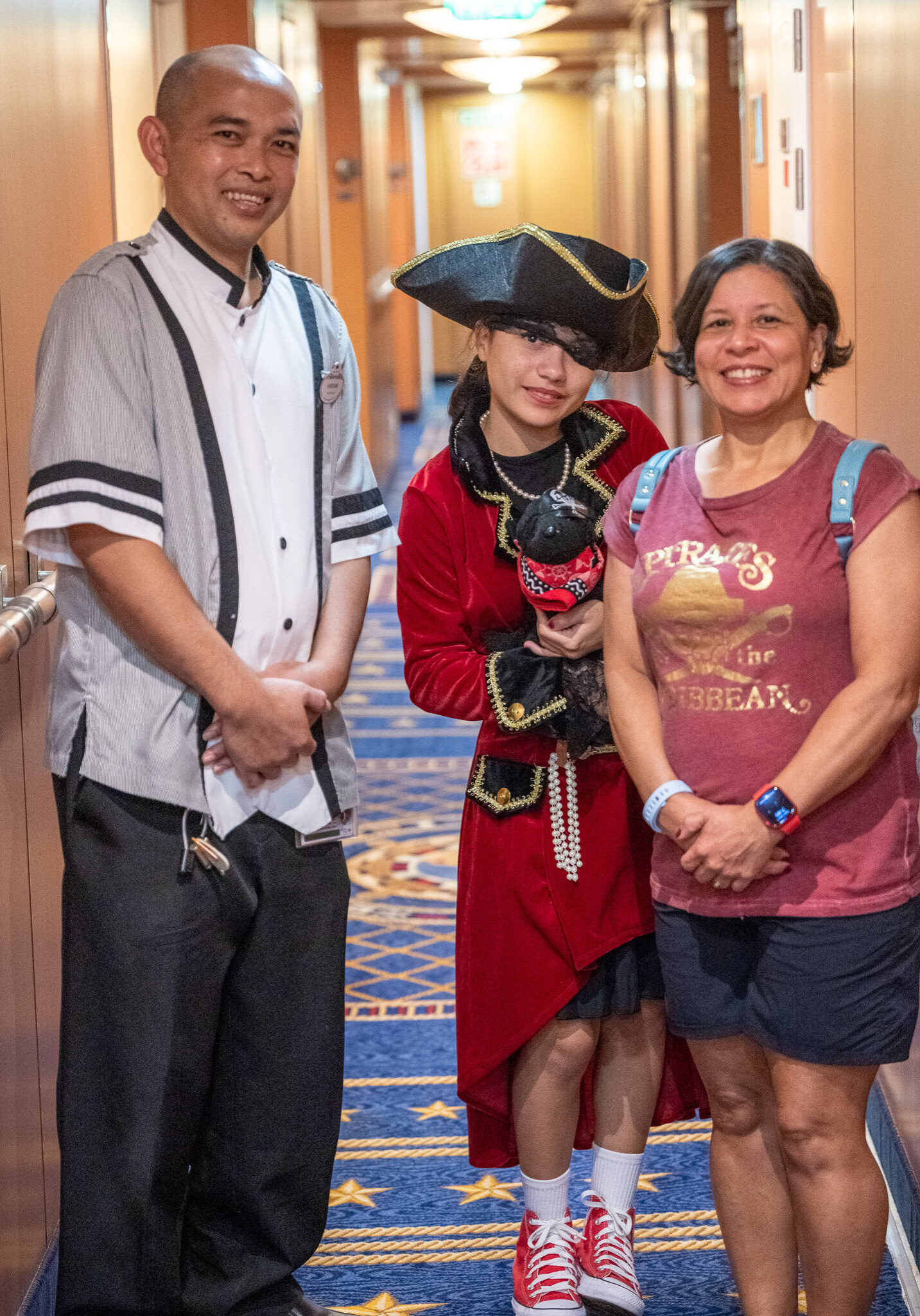 Wayan, a Disney Magic stateroom host, poses with a family in a ship hallway.