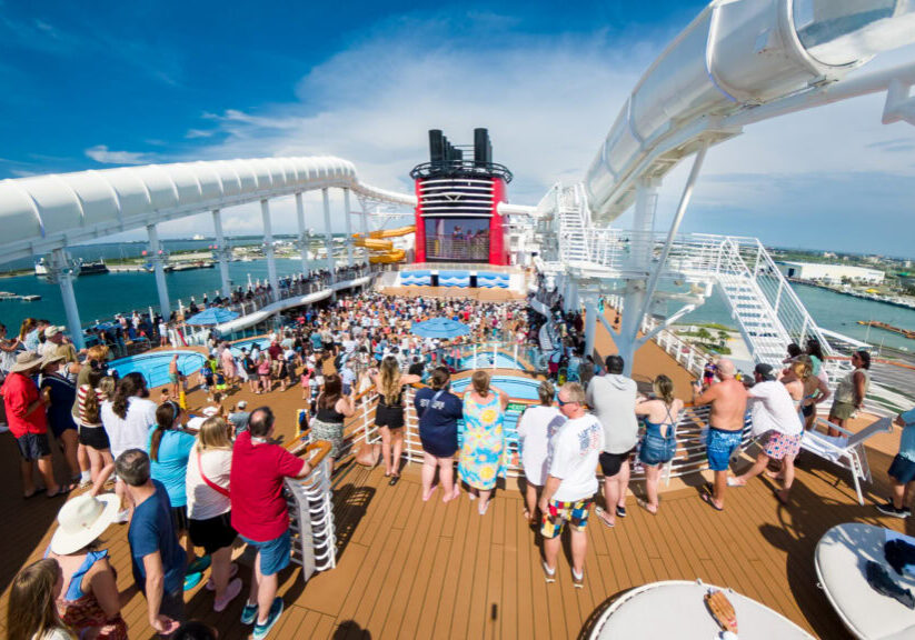 Crowds gathered on the Disney Wish upper deck during the Sail Away Party with AquaMouse slides and the ship&rsquo;s funnel in the background.