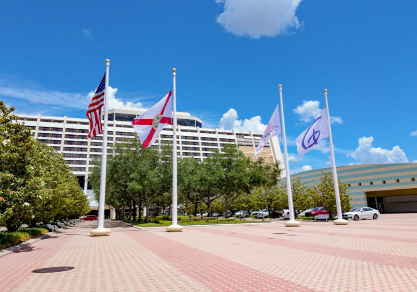 Exterior of Disney&rsquo;s Contemporary Resort with flags at the entrance under a blue sky.
