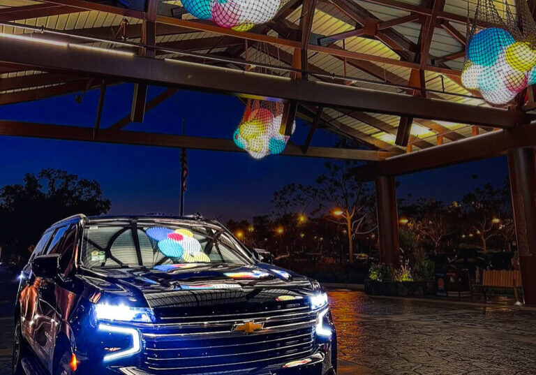 GEM Luxury Services vehicle parked at Disney’s Polynesian Resort at night, reflecting the resort's signature colorful lanterns.