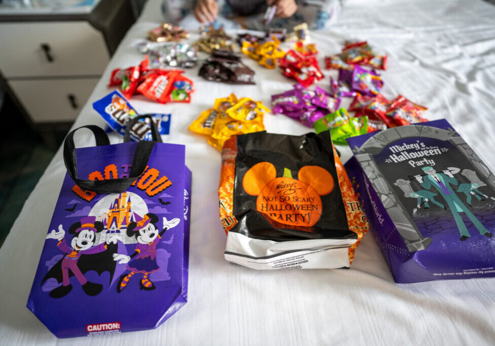 Mickey&rsquo;s Not-So-Scary Halloween Party candy spread across a bed at Disney&rsquo;s Grand Floridian Resort, with Halloween treat bags from Magic Kingdom.