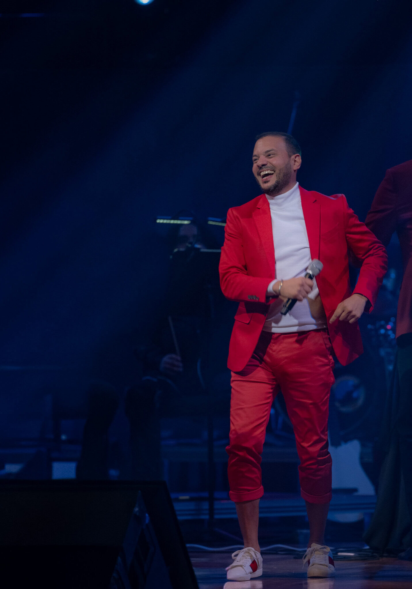 Ricardo Rosado performing live in Puerto Rico wearing a red suit during a concert with orchestra